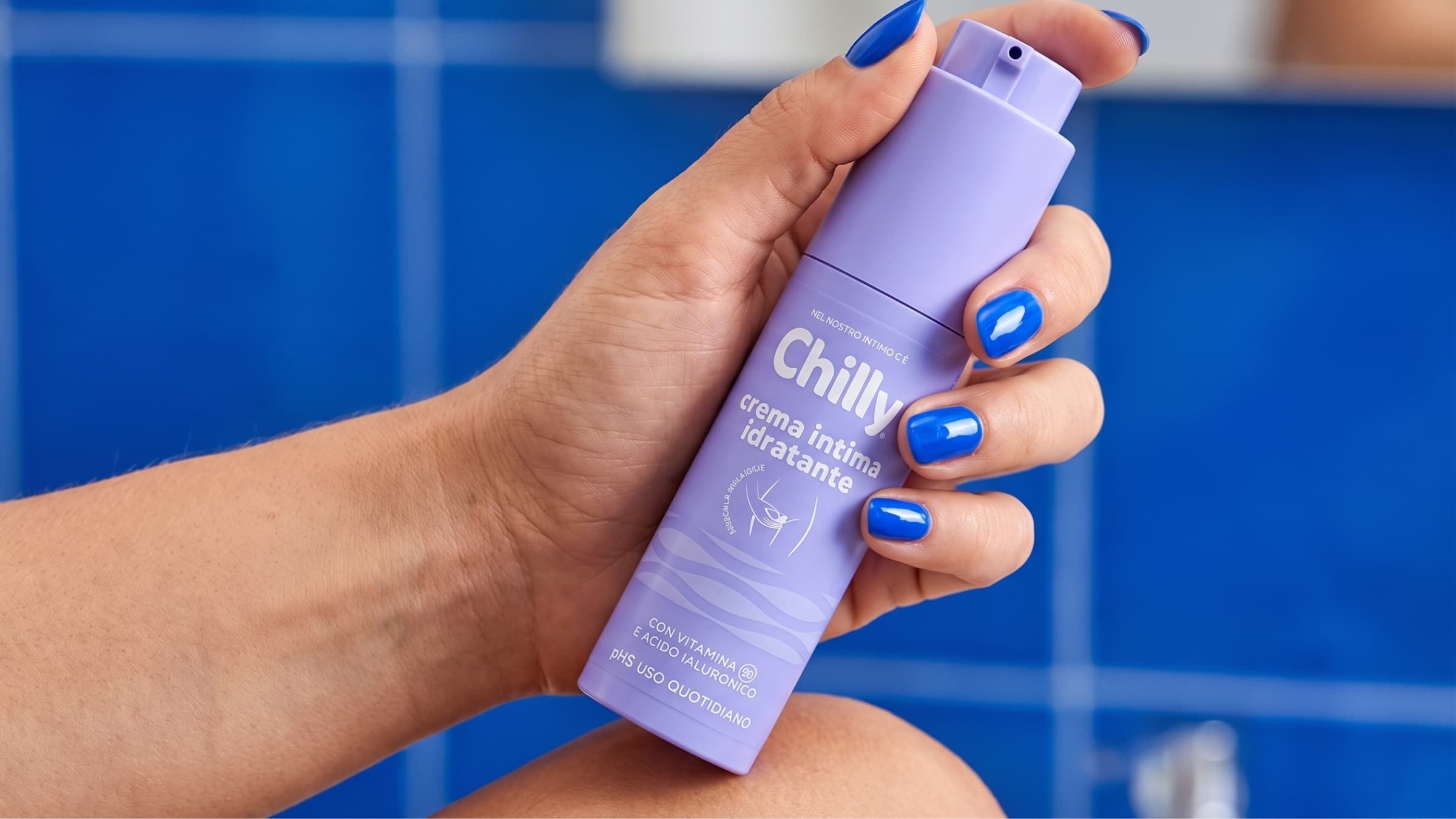 Mano con smalto blu che regge un flacone di crema Chilly su fondo blu